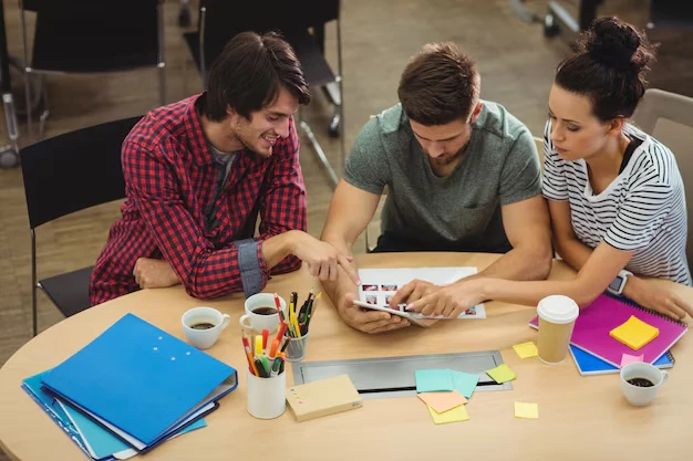 Three-people-discussing-tablet-work-desk-coffee-notes